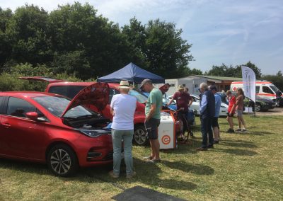 Besucher begutachten Elektroautos. Ein Auto wird über eine Mobilen Ladestation geladen