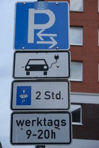 Beschilderung einer Ladesäule mit 4 Schildern. Oben Parkplatz Symbol. Darunter Piktogramm Elektroauto. Als drittes Parkscheibe für 2 Stunden. Unten Beschilderung für zeitliche Beschränkung